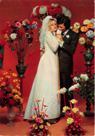 NOCES - L'époux Et La Mariée - Des Mariés Entourés De Fleurs - Murs Rouges - Colorisé - Carte Postale - Hochzeiten