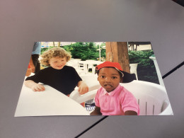 Photo  Snapshot Photo Couleur Enfant, Garçon Blond, Avec Des Cheveux Frisés Avec Un Enfant De Couleur, Assis à Une Table - Personnes Anonymes
